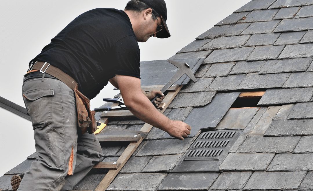 Roofer replacing a damaged section of slate on a pitched roof