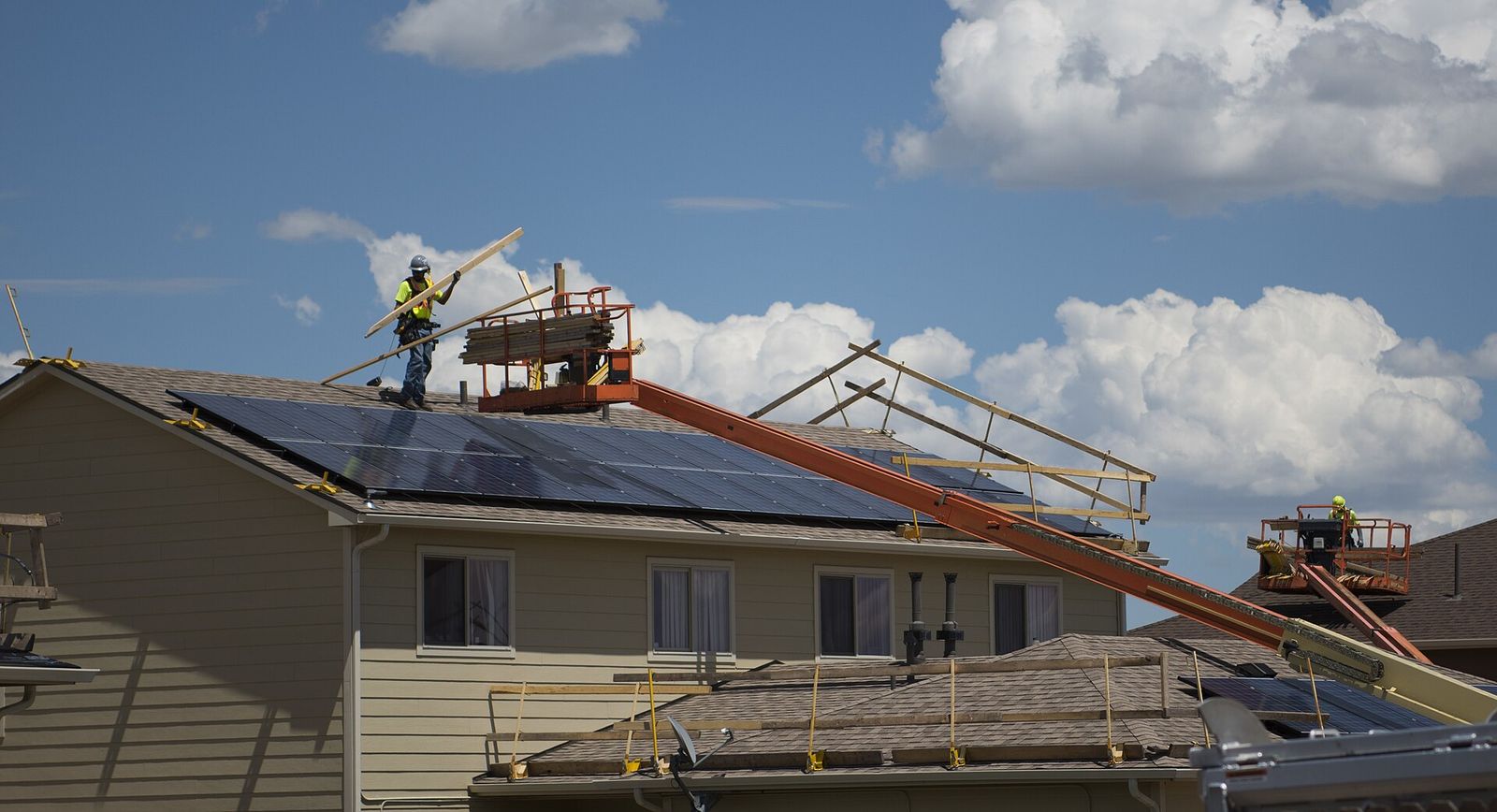 Roofers installing shingles on a long two-story roof